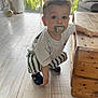 Izaia a rejoint le concours — aidez-le/la à gagner de superbes lots ! toddler, child, indoor, pacifier, striped_pants, wooden_table, flooring, curly_hair, white_shirt, window, natural_light, furniture, sneakers, crouching, person, home, plant, daylight, face, looking