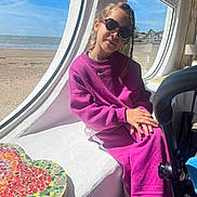 Elena participe au concours pour gagner de l'argent avec cette photo : child, girl, purple_outfit, sunglasses, window, beach, sea, sky, mosaic_table, heart_pattern, indoor, sunlight, casual_clothing, relaxing, seaside, portrait, seated, hands_folded, natural_light, cozy