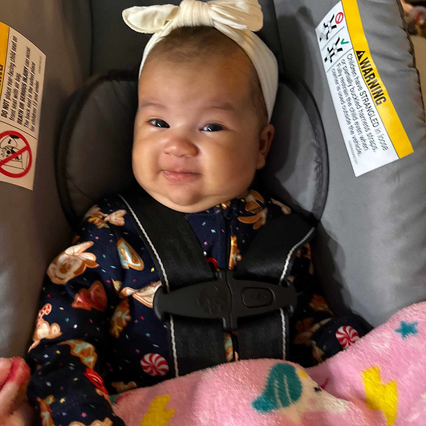 Fucshia is registered to the contest to win money with this photo: baby, child, car_seat, headband, bow, blanket, unicorn, lightning_bolt, gingerbread, candy, clothing, safety_harness, smile, face, infant, person, cute, indoor, portrait, happy