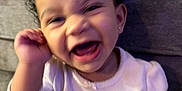Reign is registered to the contest to win money with this photo: baby, laughing, smiling, indoor, couch, child, happy, person, clothing, curly_hair, pink_blanket, home, infant, cute, portrait, sitting, white_shirt, earring, fun, joy