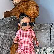 Reign is registered to the contest to win money with this photo: baby, blanket, checkered_pattern, child, couch, cozy, cute, furniture, happy, home, indoor, person, pink_clothing, playful, plush_toy, seated, smiling, sunglasses, teddy_bear, toddler