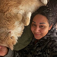 Jupiter joined the competition — help win amazing prizes! person, cat, fluffy_cat, orange_cat, white_paws, smiling, selfie, cozy, lying_down, camo_hoodie, relaxed, indoor, bed, pillow, close_up, face, pet, comfort, warm_tones, casual