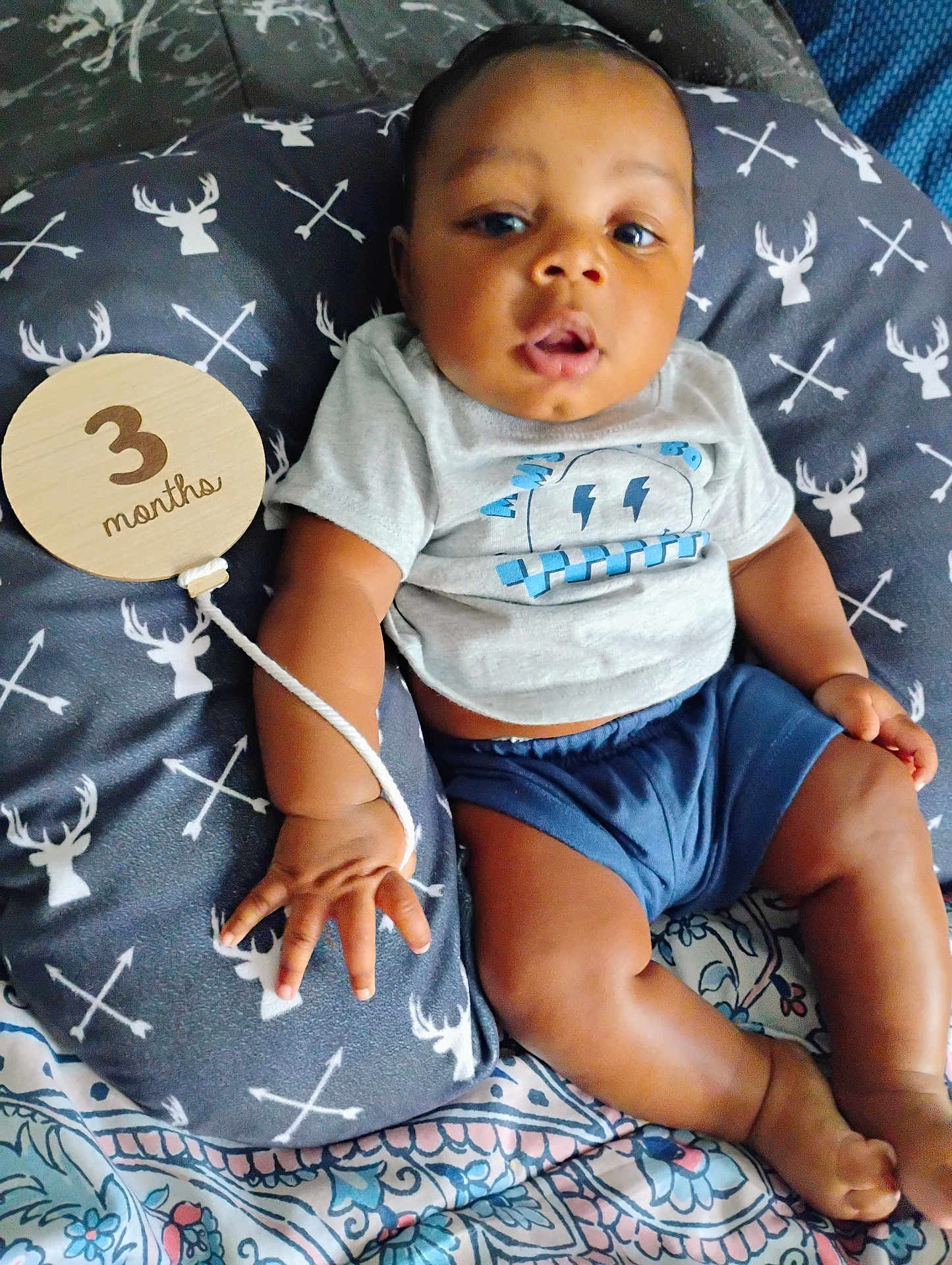 Atoka joined the competition — help win amazing prizes! baby, infant, child, pillow, clothing, tshirt, shorts, hand, foot, face, pattern, wooden_sign, text, blue, gray, bedspread, cute, young, lying_down, indoors