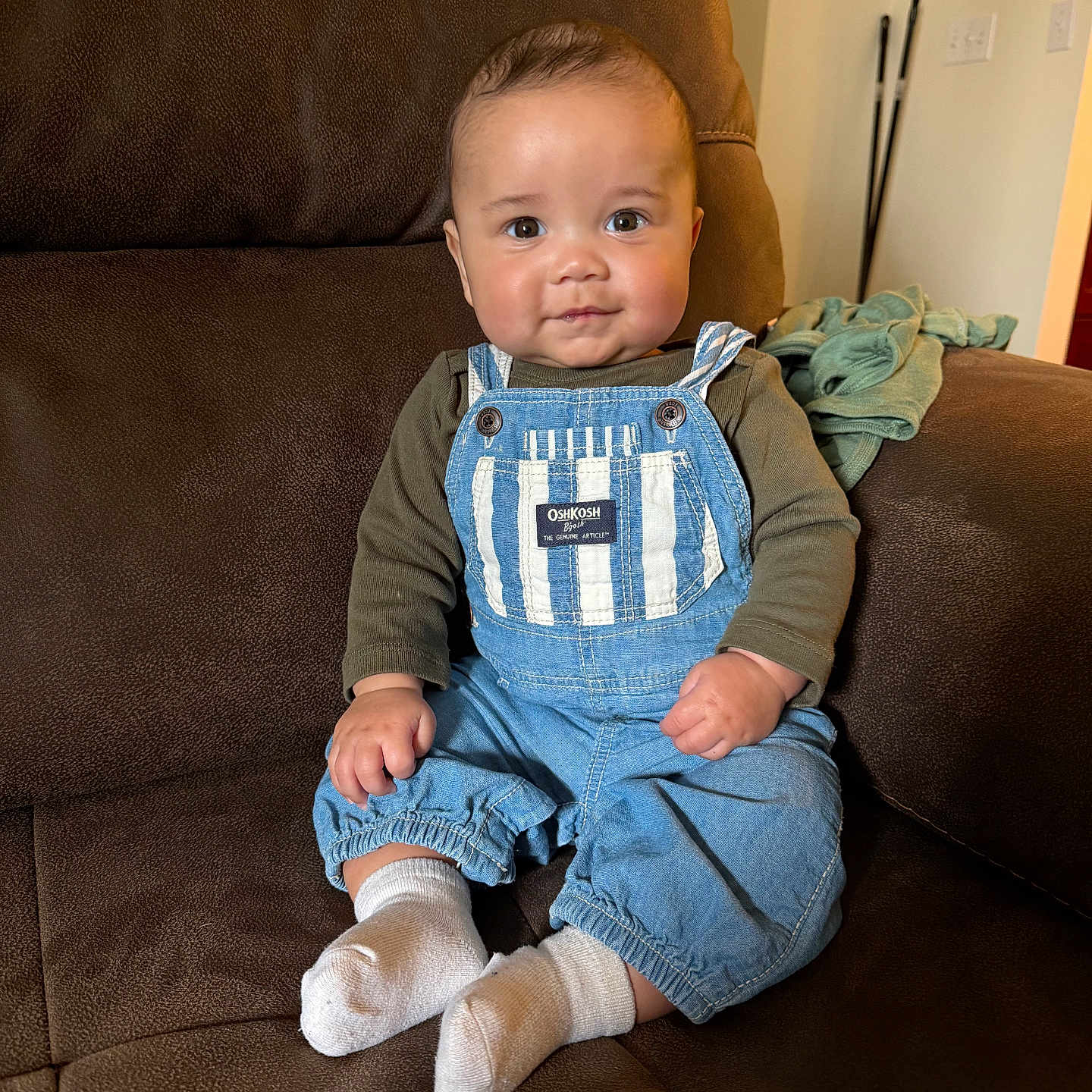 Everett is registered to the contest to win money with this photo: baby, child, infant, overalls, blue, striped, socks, couch, brown, indoor, smiling, cute, person, seated, clothing, furniture, portrait, young, happy, cozy
