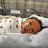 Everett is registered to the contest to win money with this photo: newborn, baby, incubator, hospital, medical_tube, onesie, lion_pattern, face, lying_down, infant, bed, blanket, healthcare, patient, cute, small, child, indoors, portrait, treatment