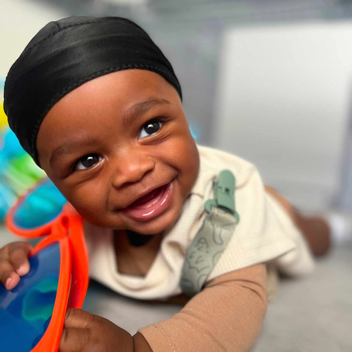 Alijah joined the competition — help win amazing prizes! accessory, baby, bright, child, closeup, clothing, cute, expression, face, hand, happy, head_wrap, indoors, infant, lying_down, portrait, skin, smiling, sunglasses, toy