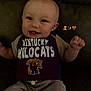 Ryker is registered to the contest to win money with this photo: baby, child, smile, happy, sitting, clothing, shirt, wildcats, kentucky, couch, furniture, face, head, infant, cute, indoor, person, young, small, casual