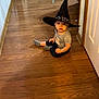 Liam Mateo joined the competition — help win amazing prizes! baby, casual_clothing, child, curious, cute, dark_pants, expression, floor, gray_shirt, hat, hat_decorations, home, indoor, pacifier, person, sitting, toddler, witch_hat, wooden_floor, young_child