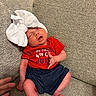 baby, newborn, infant, sleeping, bow, headwear, red_shirt, blue_shorts, couch, fabric, hand, peaceful, indoors, skin, person, clothing, textile, seated, small, cute