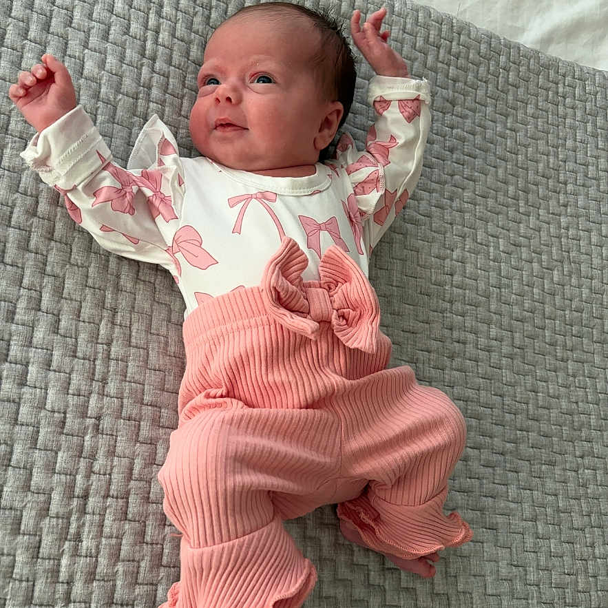 Mary is registered to the contest to win money with this photo: baby, infant, pink_clothing, white_clothing, blanket, textured_blanket, lying_down, raised_arms, cute, small_hands, newborn, indoors, portrait, child, soft_lighting, comfortable, resting, smiling, cozy, adorable