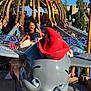 child, smiling, amusement_park, ride, dumbo, elephant, mouse_ears, blue_sky, outdoor, fun, playful, joy, toy, colorful, sunlight, theme_park, young_child, happy, entertainment, vacation