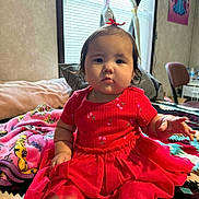 Sara is registered to the contest to win money with this photo: baby, child, red_dress, blanket, indoor, furniture, chair, poster, curtains, window, person, face, foot, hand, expression, room, decor, colorful, sitting, cozy