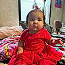 baby, child, red_dress, blanket, indoor, furniture, chair, poster, curtains, window, person, face, foot, hand, expression, room, decor, colorful, sitting, cozy