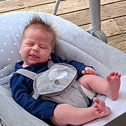 Simon joined the competition — help win amazing prizes! baby, infant, child, baby_seat, cushion, wooden_deck, blue_clothing, gray_harness, sheep_design, closed_eyes, tongue_out, bare_feet, spiky_hair, playful_expression, outdoor, daylight, cute, relaxed, person, infant_care