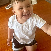 Julian is registered to the contest to win money with this photo: toddler, child, smiling, white_tshirt, shorts, kneeling, wooden_floor, indoor, happy, cute, person, young_child, home, casual_clothing, short_hair, bright, flooring, cheerful, portrait, natural_light