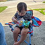 toddler, child, toy, chair, outdoor, concrete, driveway, street, sunny, curious, casual, daytime, shorts, shirt, footwear, plastic, playtime, suburban, grass, relaxed