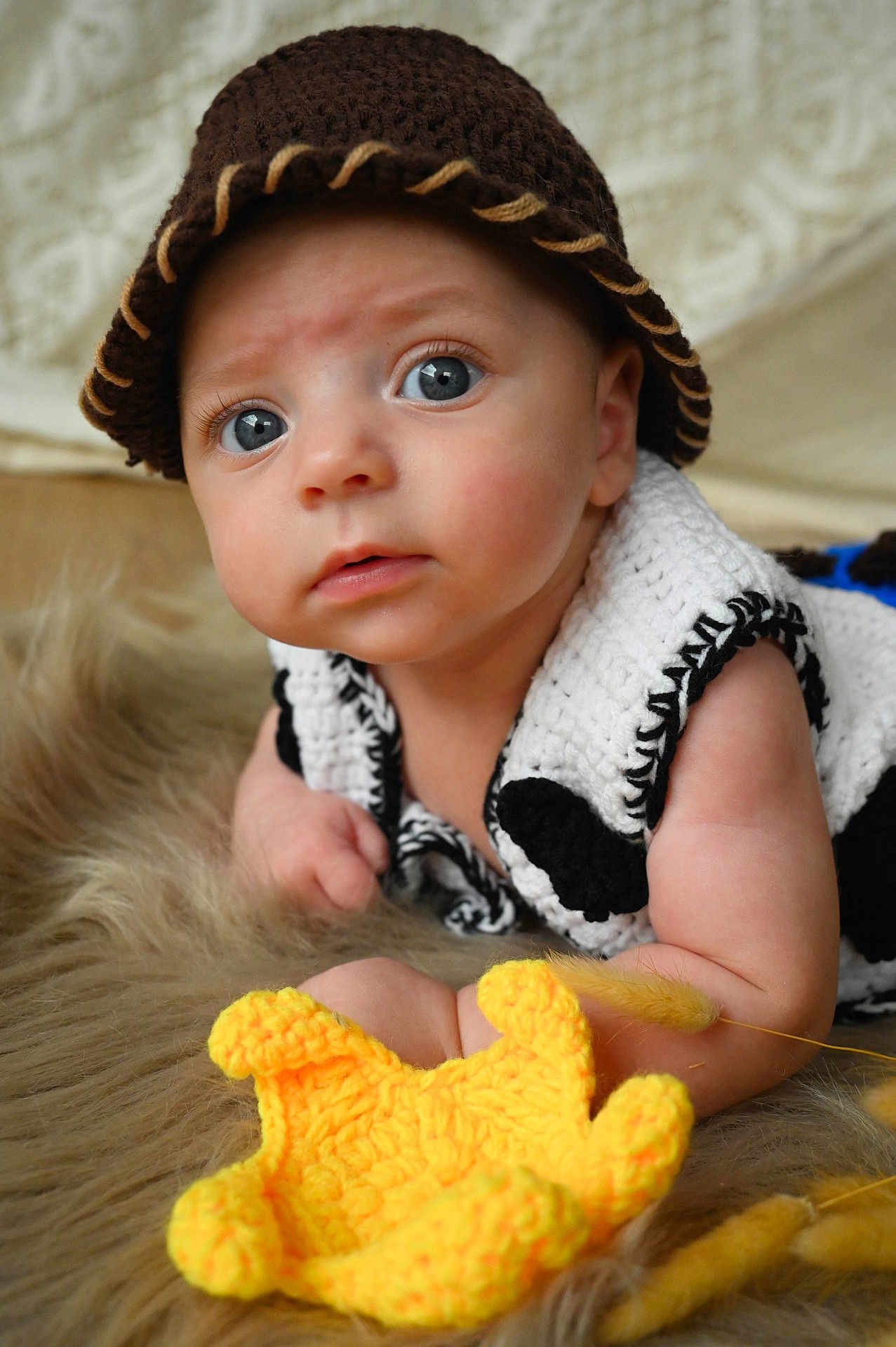 Victor a rejoint le concours — aidez-le/la à gagner de superbes lots ! baby, infant, crocheted_hat, blue_eyes, curious, knitted_outfit, white, black, yellow_toy, furry_surface, closeup, portrait, child, cute, soft_texture, indoor, hands, face, expression, lying_down
