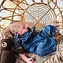 baby, sleeping, denim_overalls, striped_shirt, wicker_chair, fluffy_cushion, teddy_bear, knitted_toy, cozy, indoor, child, cute, resting, soft_fabric, infant, portrait, relaxation, cuddly, home, peaceful