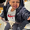 child, girl, toddler, portrait, smiling, outdoor, stroller, sitting, red_bows, braids, jacket, shirt, necklace, earrings, shoes, sunlight, sidewalk, garden, leaves, photography