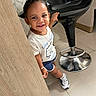 Khloe joined the competition — help win amazing prizes! child, toddler, smiling, portrait, indoors, salon, chair, barber_chair, black_chair, wooden_panel, tile_floor, white_shirt, blue_shorts, sneakers, necklace, bracelet, hair_bow, standing, happy, fashion