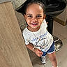 Khloe joined the competition — help win amazing prizes! child, toddler, smiling, portrait, indoors, salon, salon_chair, hair_bun, earrings, necklace, bracelet, white_shirt, blue_shorts, sneakers, standing, wooden_counter, tile_floor, black_chair, happy, photograph