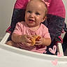 baby, high_chair, pink_clothing, toy, duck_toy, smiling, child, indoor, face, hair_bow, cute, happy, person, seat, infant, cheerful, portrait, holding, pink, playful
