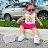 child, toddler, outdoor, sitting, sunglasses, pink_clothing, pink_shorts, hair_bows, braided_hair, sneakers, handbag, pearl_handle, capybara_shirt, car, suv, grass, curb, house, tree, blue_sky