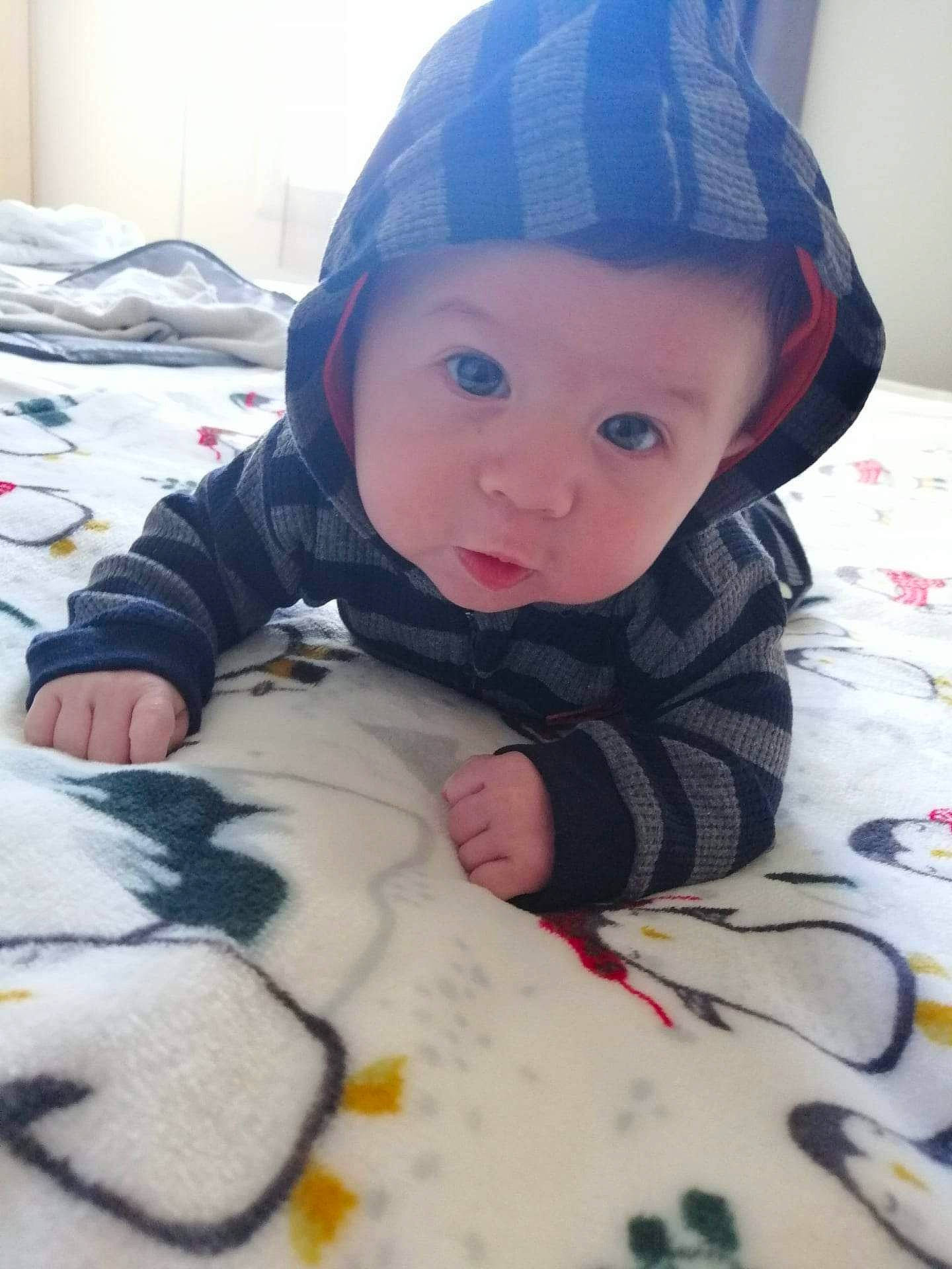 Aiden participe au concours pour gagner de l'argent avec cette photo : baby, baby_toddler_clothing, beanie, bed_sheet, bedding, cap, cheek, child, comfort, fashion_accessory, flooring, fur, headwear, knit_cap, linens, pattern, person, sitting, skin, sleeve