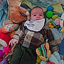 Yann participe au concours pour gagner de l'argent avec cette photo : baby, infant, toy, stuffed_animal, mickey_mouse, clothing, bib, plush_toy, colorful, patterned, child, smiling, indoor, blanket, play_area, soft_toys, person, cute, lying_down, fabric