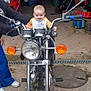 baby, motorcycle, garage, person, smile, toy, wheel, handlebar, headlight, clothing, footwear, hand, mirror, concrete, vehicle, adult, storage, equipment, sitting, child
