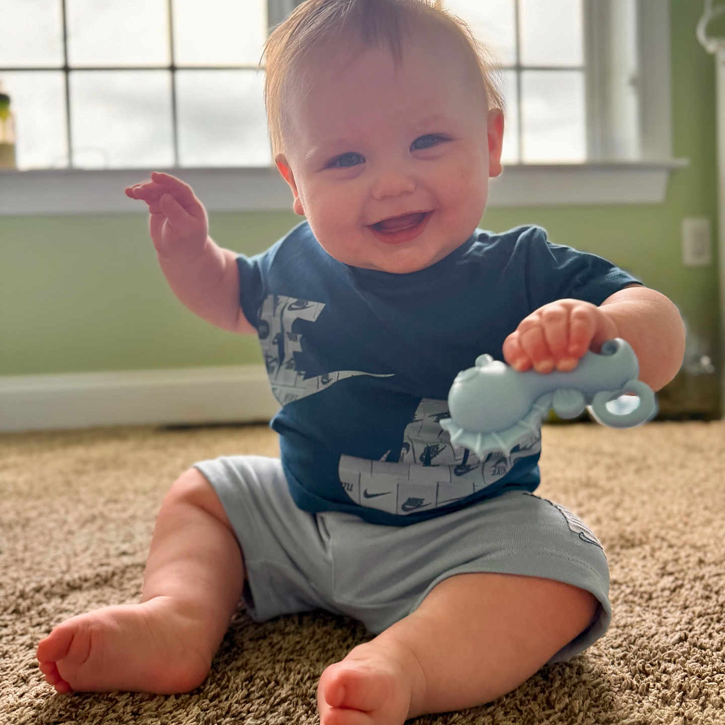 Grayson is registered to the contest to win money with this photo: baby, blue_shirt, carpet, child, cute, foot, green_wall, hand, happy, home, indoor, infant, person, playing, portrait, shorts, sitting, smiling, toy, window