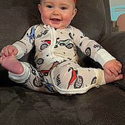 Stella is registered to the contest to win money with this photo: child, baby, infant, bow, headband, smile, onesie, motorcycle_print, foot, hand, recliner, chair, home, portrait, happy, cute, clothing, furniture, blue_eyes, playful