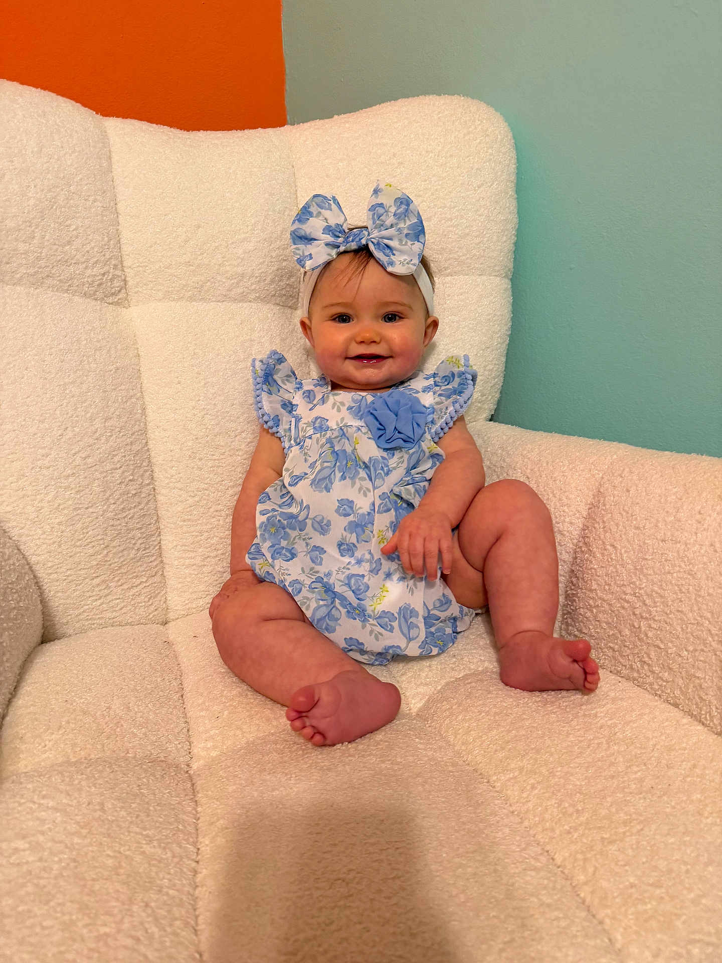 Stella joined the competition — help win amazing prizes! baby, infant, child, bow_headband, floral_dress, blue_dress, white_chair, armchair, smiling, toes, legs, face, cozy, nursery, pastel_wall, orange_wall, teal_wall, portrait, sitting, barefoot