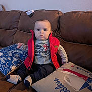 Jacob joined the competition — help win amazing prizes! baby, child, red_vest, gray_shirt, socks, brown_couch, pillow, blue_pillow, beige_pillow, indoor, seated, person, cute, home, furniture, portrait, expressionless, comfortable, casual_clothing, young_child