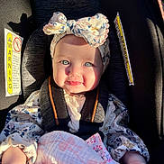 Melanie is registered to the contest to win money with this photo: baby, child, car_seat, headband, bow, blanket, smile, face, sitting, sunlight, shadow, clothing, infant, safety_harness, cute, portrait, indoor, person, happy, flower_pattern