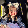 baby, child, car_seat, headband, bow, blanket, smile, face, sitting, sunlight, shadow, clothing, infant, safety_harness, cute, portrait, indoor, person, happy, flower_pattern