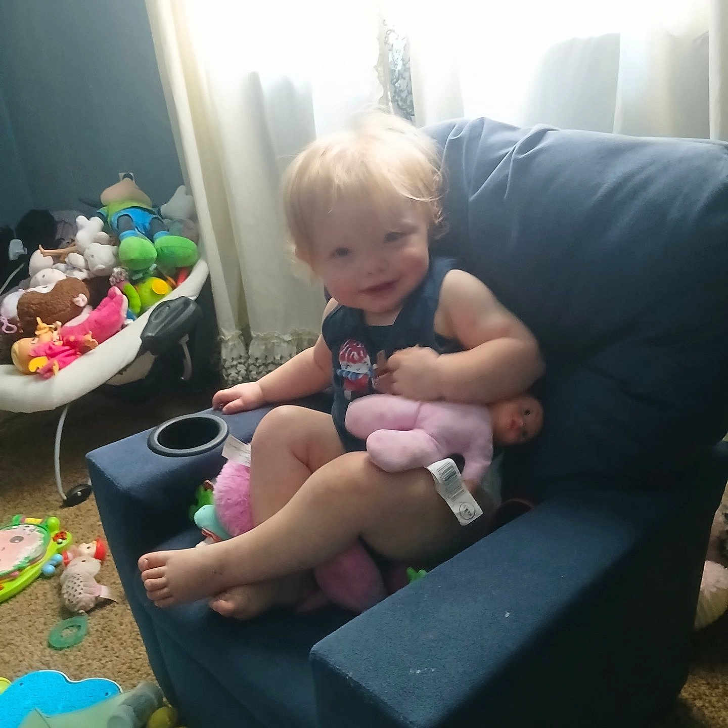 Stormie Blair joined the competition — help win amazing prizes! armchair, baby, blue_chair, carpet, child, clothing, curtains, doll, furniture, home, indoor, person, pink_doll, playtime, relaxing, smiling, stuffed_animals, toddler, toys, window