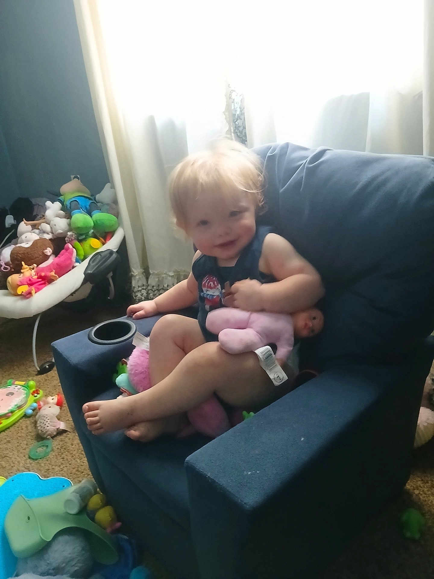 Stormie Blair joined the competition — help win amazing prizes! toddler, child, armchair, blue_chair, doll, pink_doll, toys, stuffed_animals, carpet, curtains, window, smiling, indoor, baby, clothing, person, playtime, furniture, home, relaxing