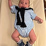 baby, infant, striped_onesie, blue_shoes, white_socks, cushioned_surface, raised_arm, black_sweater, comfortable, cute, lying_down, indoor, small_person, child, footwear, casual_clothing, smiling, portrait, human, adorable