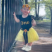 Hazel is registered to the contest to win money with this photo: toddler, child, girl, yellow_tutu, black_shirt, sunflower, headband, outdoor, bridge, railing, trees, sunlight, shadow, smiling, white_shoes, grass, park, nature, cute, happy