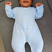 Aarav joined the competition — help win amazing prizes! baby, infant, blue_onesie, teddy_bear_design, smiling, lying_down, couch, gray_couch, plush_toy, remote_control, carpet, happy, raised_arms, indoors, person, footwear, toes, knitted_clothing, cute, portrait