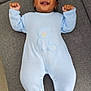 baby, infant, blue_onesie, teddy_bear_design, smiling, lying_down, couch, gray_couch, plush_toy, remote_control, carpet, happy, raised_arms, indoors, person, footwear, toes, knitted_clothing, cute, portrait