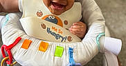 Saage joined the competition — help win amazing prizes! baby, baby_seat, bib, child, clothing, colorful, cute, face, feeding, happy, indoor, infant, joyful, person, playful, ribbons, sitting, smile, toy, young_child