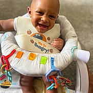 Saage is registered to the contest to win money with this photo: baby, smiling, bib, baby_seat, toys, ribbons, happy, child, infant, indoor, playful, colorful, person, cute, young, seat, clothing, expression, face, feeding