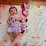 baby, infant, smiling, purple_clothing, headband, toy, minnie_mouse, plush_toy, milestone_blanket, floral_pattern, floor, wooden_floor, lying_down, cute, child, playtime, indoors, happy, person, three_months