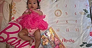 Violet is registered to the contest to win money with this photo: baby, barbie_doll, barbie_pillow, carpet, child, clothing, colorful, cute, decorative, floral_pattern, headband, indoors, infant, lying_down, milestone_blanket, month_marker, pink_tutu, playtime, portrait, toy_packaging