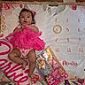 Violet is registered to the contest to win money with this photo: baby, pink_tutu, headband, milestone_blanket, floral_pattern, carpet, barbie_pillow, barbie_doll, toy_packaging, infant, clothing, lying_down, indoors, cute, child, portrait, month_marker, colorful, playtime, decorative
