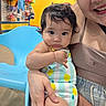 Violet joined the competition — help win amazing prizes! baby, blue_chair, casual, child, clothing, colorful, curly_hair, cute, face, happy, holding, indoor, pattern, person, playful, shopping_area, smile, swimsuit, woman, yellow_wall