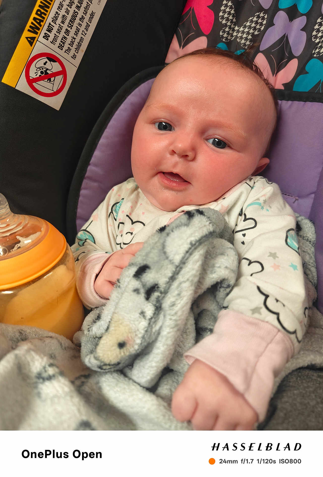 Elena is registered to the contest to win money with this photo: baby, infant, blanket, car_seat, bottle, patterned_background, cute, child, indoor, close_up, soft_texture, clothing, face, hands, expression, comfort, warmth, portrait, newborn, seat