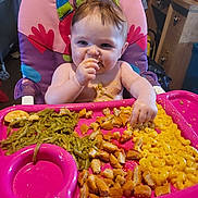 Luna joined the competition — help win amazing prizes! baby, high_chair, food, green_beans, chicken_nuggets, macaroni_and_cheese, messy, eating, child, indoor, pink_tray, face, hand, smile, hair, plate, kitchen, person, seat, happy